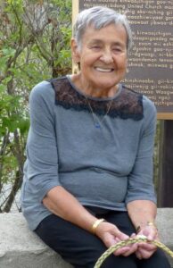An elder with short grey hair and a lovely smile sits holding a braid of sweetgrass.