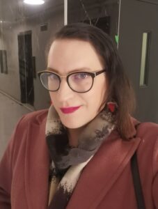 A white-presenting woman with glasses and a red coat smiling into the camera.